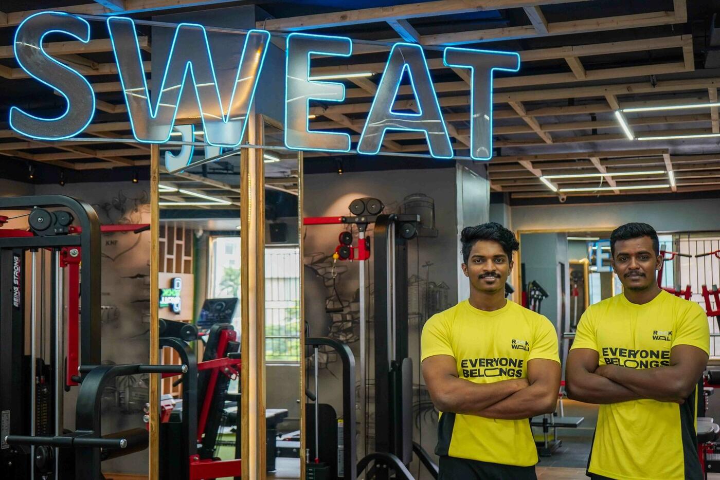 Trainers in Everyone Belongs tees under the neon sweat sign